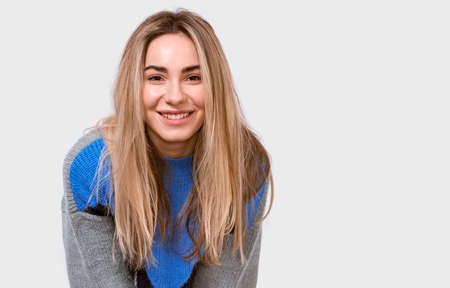 Charming friendly-looking European young woman in stylish loose sweater, smiling broadly and looking to the camera, isolated over white background. People emotions conceptの写真素材