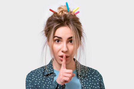 Funny beautiful young woman with wild hair and colorful markers in hair, holding her index finger to...