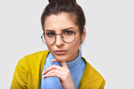 Serious young businesswoman wearing blue blouse and round transparent eyeglasses, with white blank...