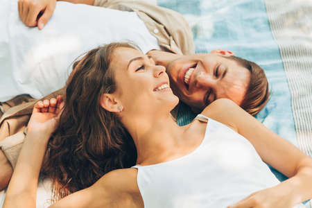 Top view of beautiful couple in love dating outdoors at the park on a sunny day. Couple lying on the blanket smiling and looking to each other with love. Valentine day. Happy relationshipの写真素材