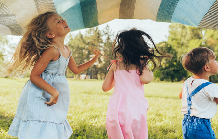 Playful children playing under the blanket, jumping and dancing together. Happy little boy and little girls enjoying summer day in the park. Cheerful kids playing outdoors. Childhood conceptの写真素材
