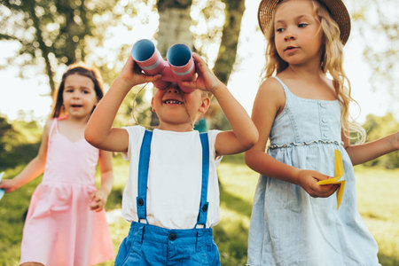 Chilldren playing with a binoculars and paper plane in summer day in park. Happy kids playing...