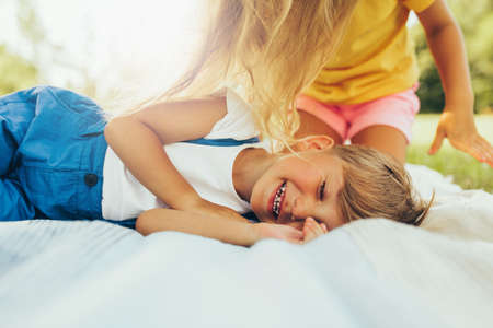 Candid image of happy children playing on the blanket outdoors. Happy little boy and cute little girl relaxing in the park. Kids having fun on sunlight. Sister and brother spending time together.の写真素材