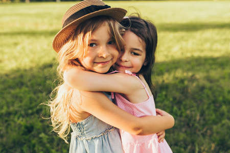 Outdoors portrait of two adorable children shares love and frienship. Two little girls playing in the park. Two sisters having fun on sunlight and nature background. Childhood and friendship conceptの写真素材