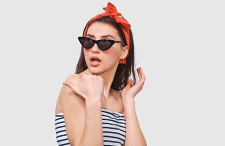 Stylish pretty young woman feeling surprised, wearing retro outfit posing over white wall. Beautiful...