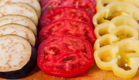Sliced eggplant tomato and sweet pepper on wooden cutting boardの写真素材