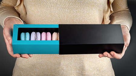 Beautiful female hands hold multicolored french macaroons in gift boxの写真素材