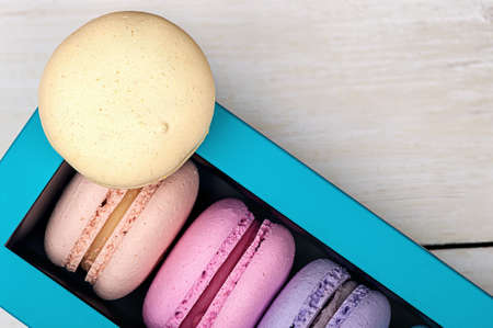 Macaroons in box and one on top on wooden backgroundの写真素材