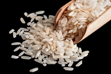 White rice in wooden scoop closeup on black backgroundの写真素材