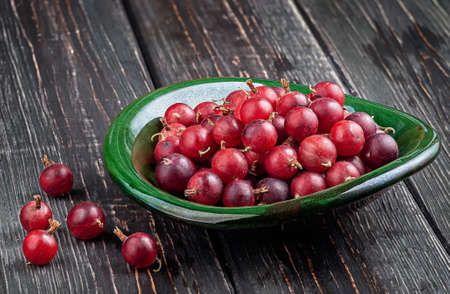 Red gooseberries on a dark table in a clay bowlの写真素材