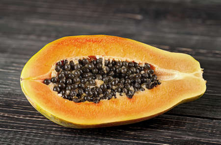 Half papaya on a wooden table. Papaya lies on dark boards with a blurred background.の写真素材