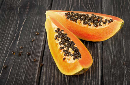Two pieces of ripe papaya on a wooden table. Quarters of papaya on a dark plank table.の写真素材