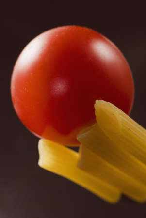 Pennette rigate and red cherry tomato on black background with selective focus. Vertical viewの写真素材