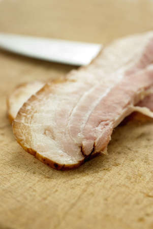Individual slice of bacon on wood table with knife in background. Selective focusの写真素材