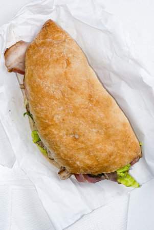 Ciabatta sandwich stuffed with meat and vegetables on white table の写真素材