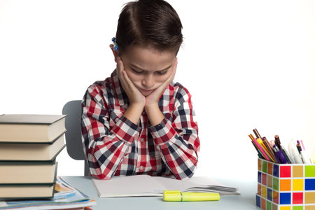 Schoolboy writing his homework. Student thinking at his desk.の写真素材