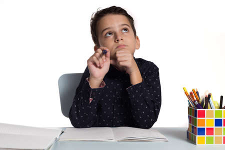 Schoolboy writing his homework. Student thinking at his desk.の写真素材