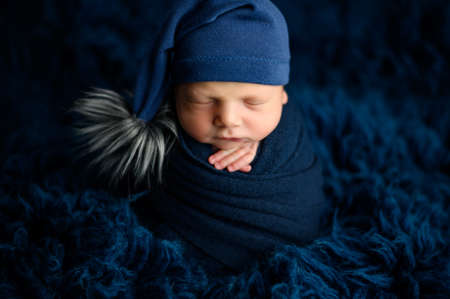 Lovely newborn baby boy sleeping wrapped pose an a blue flokati wrapped in a fluffy blue materialの写真素材