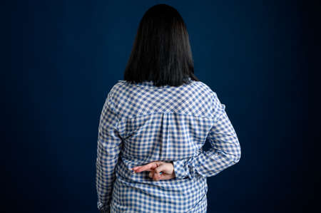 Young woman with black hair dressed casually in a blu shirt with squares showing good luck behind himの写真素材