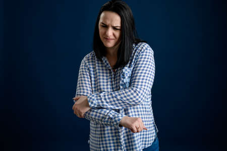 Young woman with black hair dressed casually in a blu shirt with squares has elbow painの写真素材