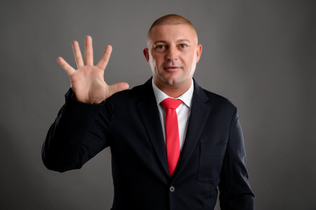 Portrait of cool businessman wearing elegant black suit and red tie showing five isolated over gray...