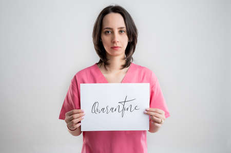Young doctor in pink dress, holding a white sheet with quarantine announcement, posing over white isolated backgroundの写真素材