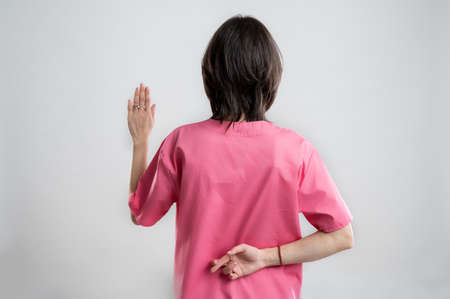 Young woman medical professional nurse or doctor dressed with pink hospital clothes, with brown hair, showing fake oath from behind posing on a white isolated backround.の写真素材