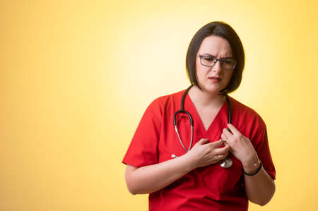 Portrait of beautiful woman doctor with stethoscope wearing red scrubs, suffering heart ache or breast pain, cardiac problems posing on a white isolated backround.の写真素材