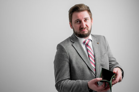 Portrait of business man wearing business clothes showing empty wallet isolated on grey background...