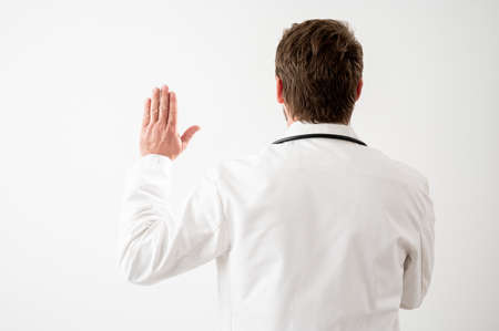Portrait of male doctor with stethoscope in medical uniform showing oath from behind posing on a white isolated backgroundの写真素材