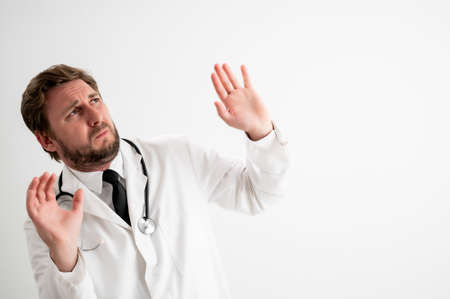 Portrait of male doctor with stethoscope in medical uniform showing fear, with her arms up posing on a white isolated backgroundの写真素材