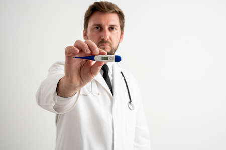 Portrait of male doctor with stethoscope in medical uniform showing digital thermometer posing on a white isolated backgroundの写真素材