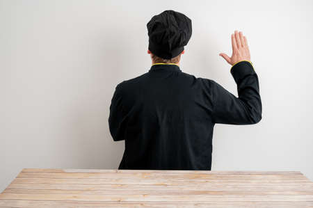 Young male chef in black uniform showing oath from behind posing on a white isolated backgroundの写真素材