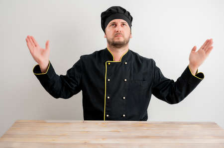 Portrait of young male chef in black uniform with open arms looking up posing on a white isolated background.の写真素材