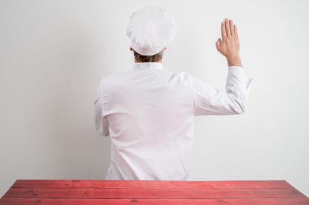 Young male chef in white uniform showing oath from behind posing on a white isolated backgroundの写真素材