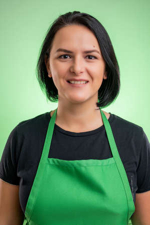 Female cook with green apron and black t-shirt, isolated on green backgroundの写真素材