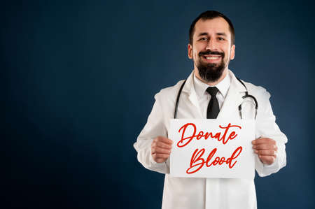 Portrait of male doctor with stethoscope in medical uniform holding a white paper and smileing posing on a blue isolated background.の写真素材