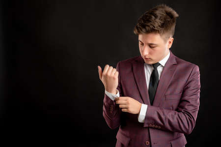 Law student with blond hair dressed in burgundy jacket, white shirt and black tie arranges his jacket posing on isolated black background with copy space advertising areaの写真素材