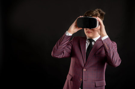 Law student with blond hair dressed in burgundy jacket, white shirt and black tie wearing virtual reality goggles posing on isolated black background with copy space advertising areaの写真素材