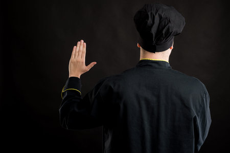 Portrait of young male dressed in a black chef suit showing oath from behind posing on a black...