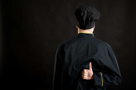 Portrait of young male dressed in a black chef suit showing thumbs up from behind posing on a black isolated background with copy space advertising areaの写真素材