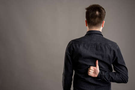 Back view of serious stylish attractive man dressed with a casual black shirt showing fingers crossed isolated on grey background with copy space advertising areaの写真素材