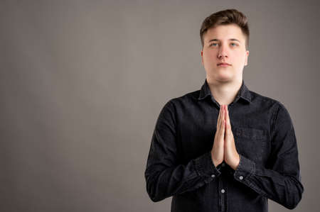 Portrait of serious stylish attractive man dressed with a casual black shirt is praying isolated on grey background with copy space advertising areaの写真素材