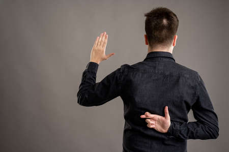 Back view of serious stylish attractive man dressed with a casual black shirt showing fingers crossed isolated on grey background with copy space advertising areaの写真素材