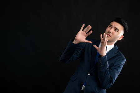 Portrait of business man wearing blue business suit and tie making scary gesture isolated on black...