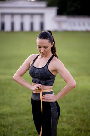Beautiful young woman, while wearing a tight sports outfit, measures her waist after doing pilates...