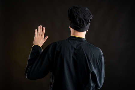 Portrait of young male dressed in a black chef suit showing oath from behind posing on a brown background with copy space advertising areaの写真素材