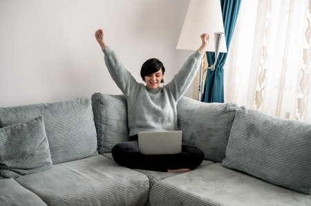 A young woman is resting on a couch with her laptop in her armsの写真素材