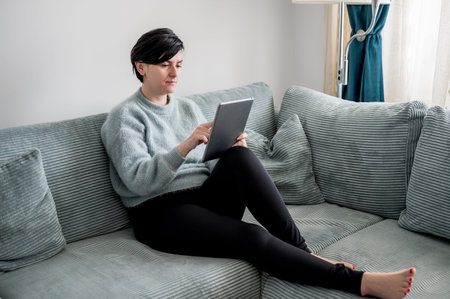 A young woman is resting on a sofa with a tablet in her arms