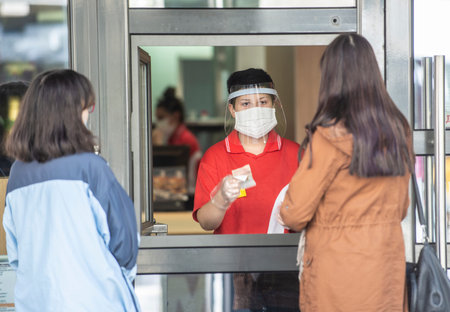 Sofia, Bulgaria - May 5th 2020: A man in mask and face shield giving the change in a kiosk. Many...